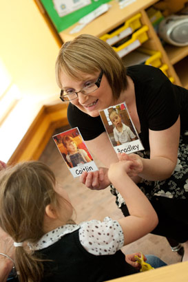 A teacher helps a young girl to
identify herself from a picture held at eye level. Taken from the teacher's point
of view