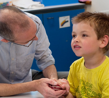 a male teacher helps a young boy
                  to learn by giving him cricket ball reward