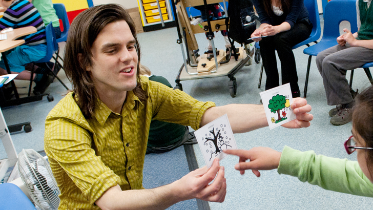 A girl points to one of two
                  picture cards held by her teacher