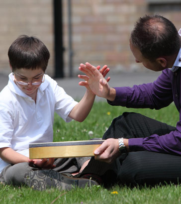 A boy and his carer sit on the grass together