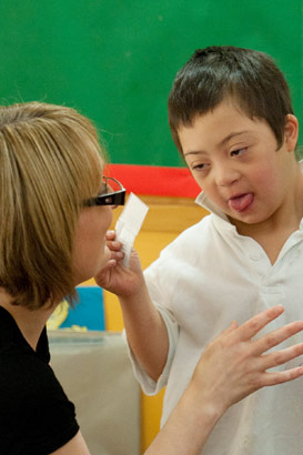 A boy standing next to a picture
                  board with his teacher