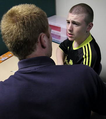 A carer  and boy sitting together on
                  the floor of a large room