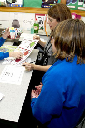 Two lead professionals sat at a classroom
                  desk with five children