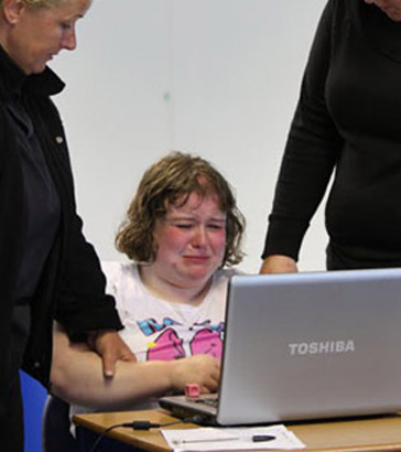 Two teachers comfort a distressed pupil
who is using a laptop