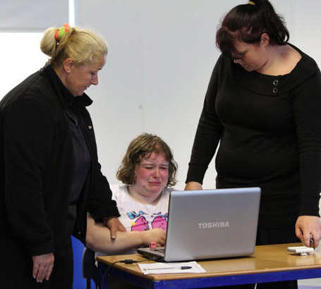 Two teachers comfort a distressed pupil
who is using a laptop