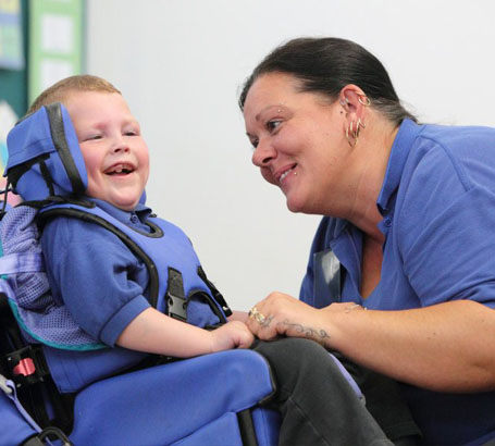 A young boy with protective headgear laughs
                  and smiles with his teacher