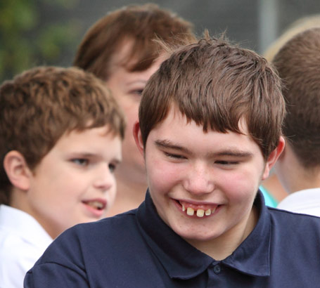 a teenage boy shakes hands with his teacher
                  in a playground full of his peers