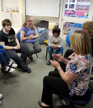 Six children and two teachers sit in a
                  circle in their classroom