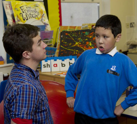 A teacher and teenage boy sat at right
                  angles to each other at a classroom table