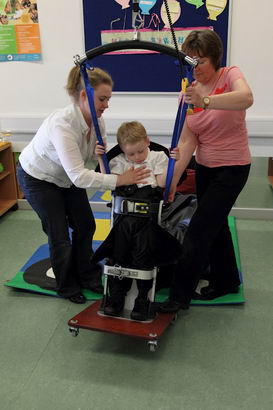 Two carers help a boy into a standing
support