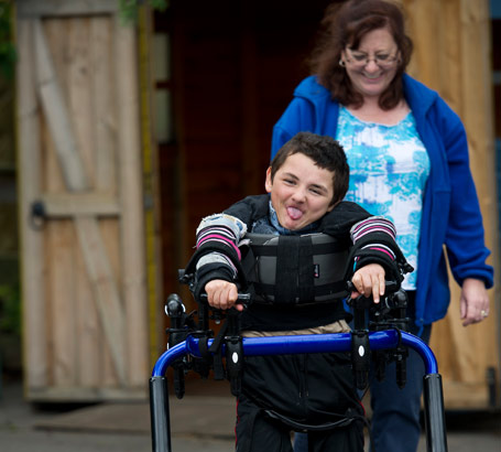 A boy in a walking support followed
                  by an adult