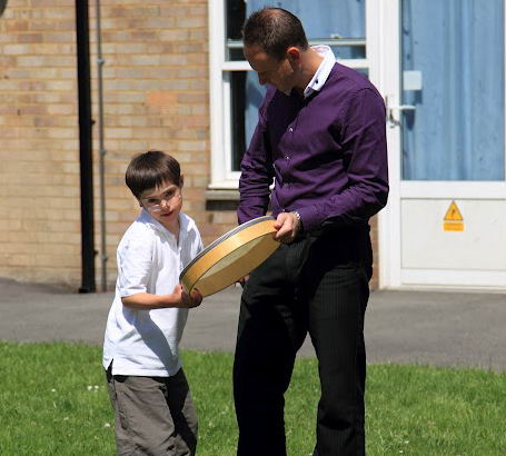 A boy and his teacher stand on the grass
with a drum