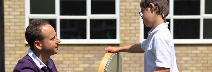 A boy holds a drum with his teacher