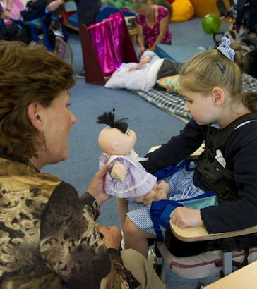 A teacher holds a doll in front
of a girl in a specialist chair