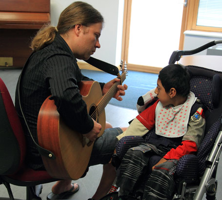 A boy watches and listens to a man play
a guitar