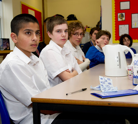 Several children sitting at a table
                  in a class