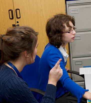 A teaching assistant helps a girl
                  at a computer