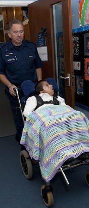 : A boy in a wheelchair, covered
in a blanket, is wheeled along a school corridor