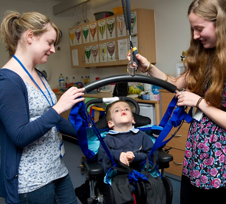 Two carers lower a boy into a wheelchair
using a hoist