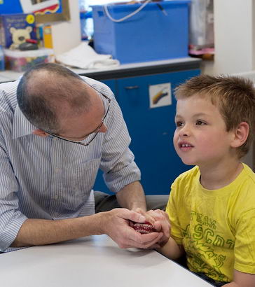 A boy holds a small cricket ball
                  with his teacher