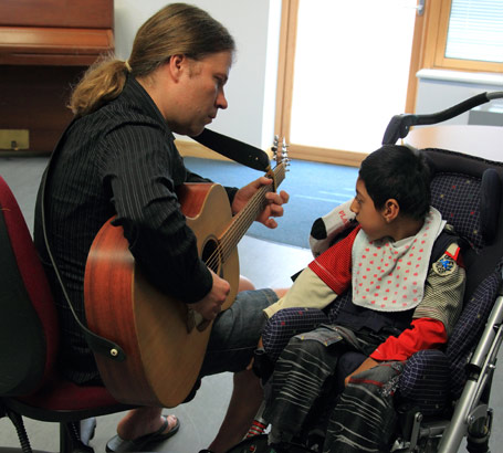 A boy watches and listens to a man play
                  a guitar