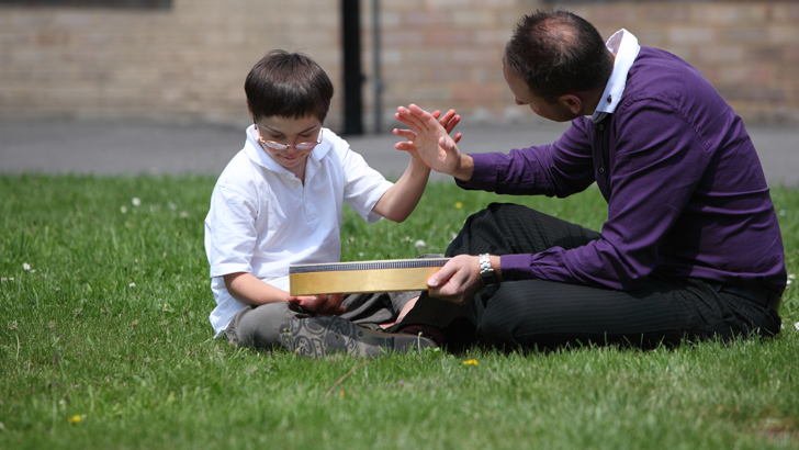 A boy and a therapist sit on
the grass with a large drum