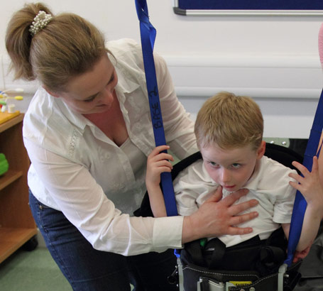 A boy being lifted into a standing frame