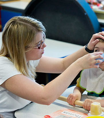 A carer helps a boy to drink from
                  a cup