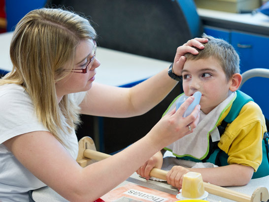 A carer helps a boy to drink from
                  a cup