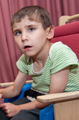 A boy in a seat holds his teacher's
                  hand