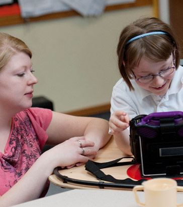 A teacher watches a girl use a communication
                  device