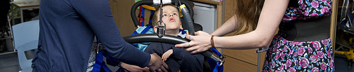 A boy being lifted out of a wheelchair
with a hoist