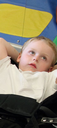 A carer helps a boy into a standing frame