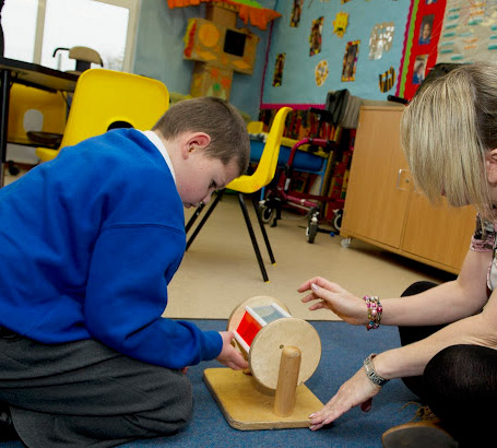 Teacher helping a boy play with
                  a toy