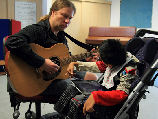 Disabled boy listening to a carer playing
the guitar.