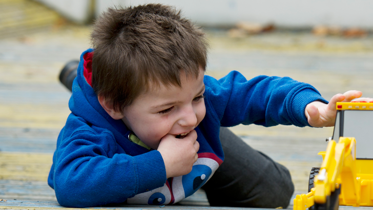 A smiling boy lies on the ground
playing with a toy digger