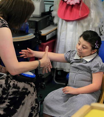 A girl sitting opposite her teacher reaches
                  out with her hand