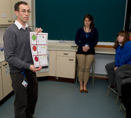 A science teacher stands in front
of his class holding up a self-assessment card