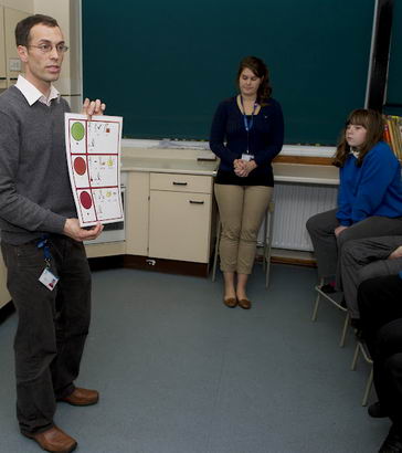 A science teacher stands in front
                  of his class holding up a self-assessment card