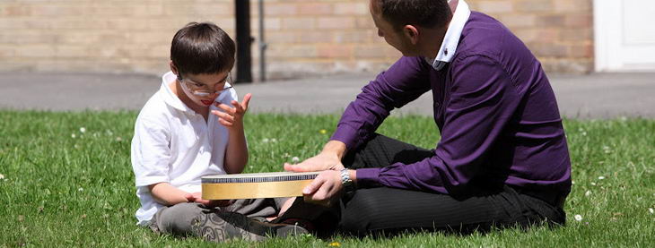 A teacher and a boy sit on the grass with
a large drum