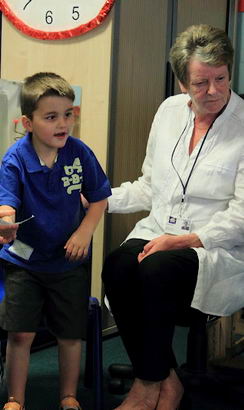 A boy stands between two seated adults,
                  holding a piece of paper